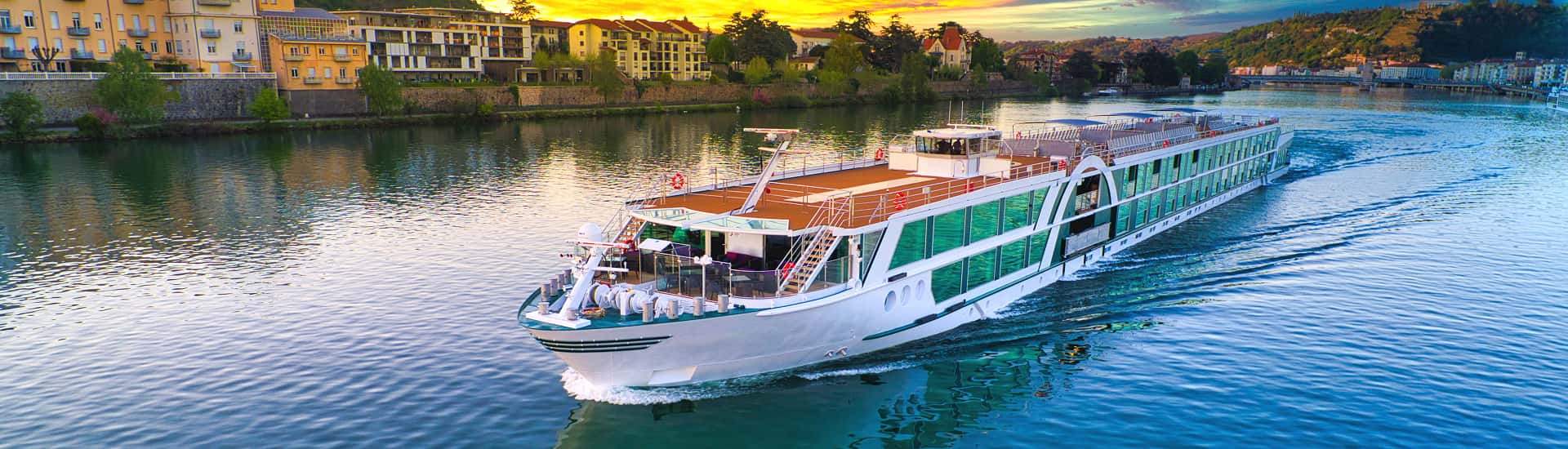 Luxuriöses Flusskreuzfahrtschiff auf einem ruhigen Fluss, umgeben von historischen Gebäuden und malerischer Landschaft bei Sonnenuntergang