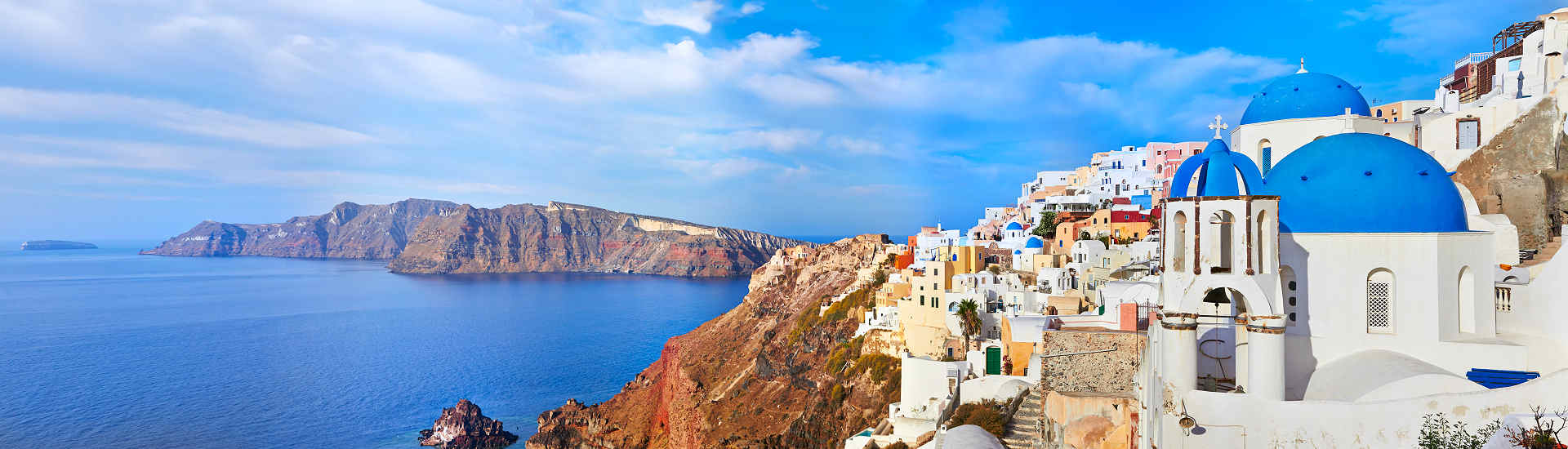 Panoramablick auf das malerische Dorf Oia auf der Insel Santorini, Griechenland, mit weißen Häusern und blauen Kuppeln, die auf einer Klippe über dem Ägäischen Meer thronen.