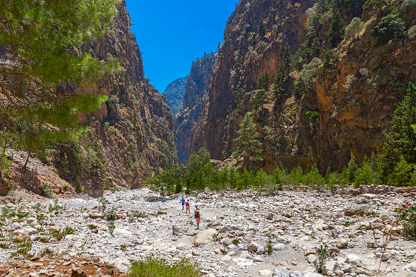 Wanderer in der Samaria-Schlucht auf Kreta, umgeben von steilen Felswänden und üppiger Natur