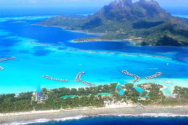 Strahlend blaue Lagune und luxuriöse Überwasser-Bungalows vor dem Hintergrund üppiger grüner Berge in Bora Bora, Ozeanien.